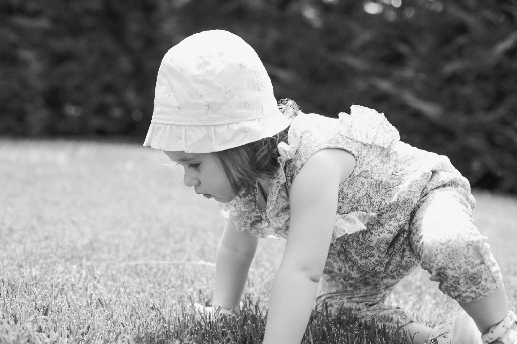 Bimba con cappellino gattona sull'erba del giardino, servizio fotografico bambini all'aperto in bianco e nero