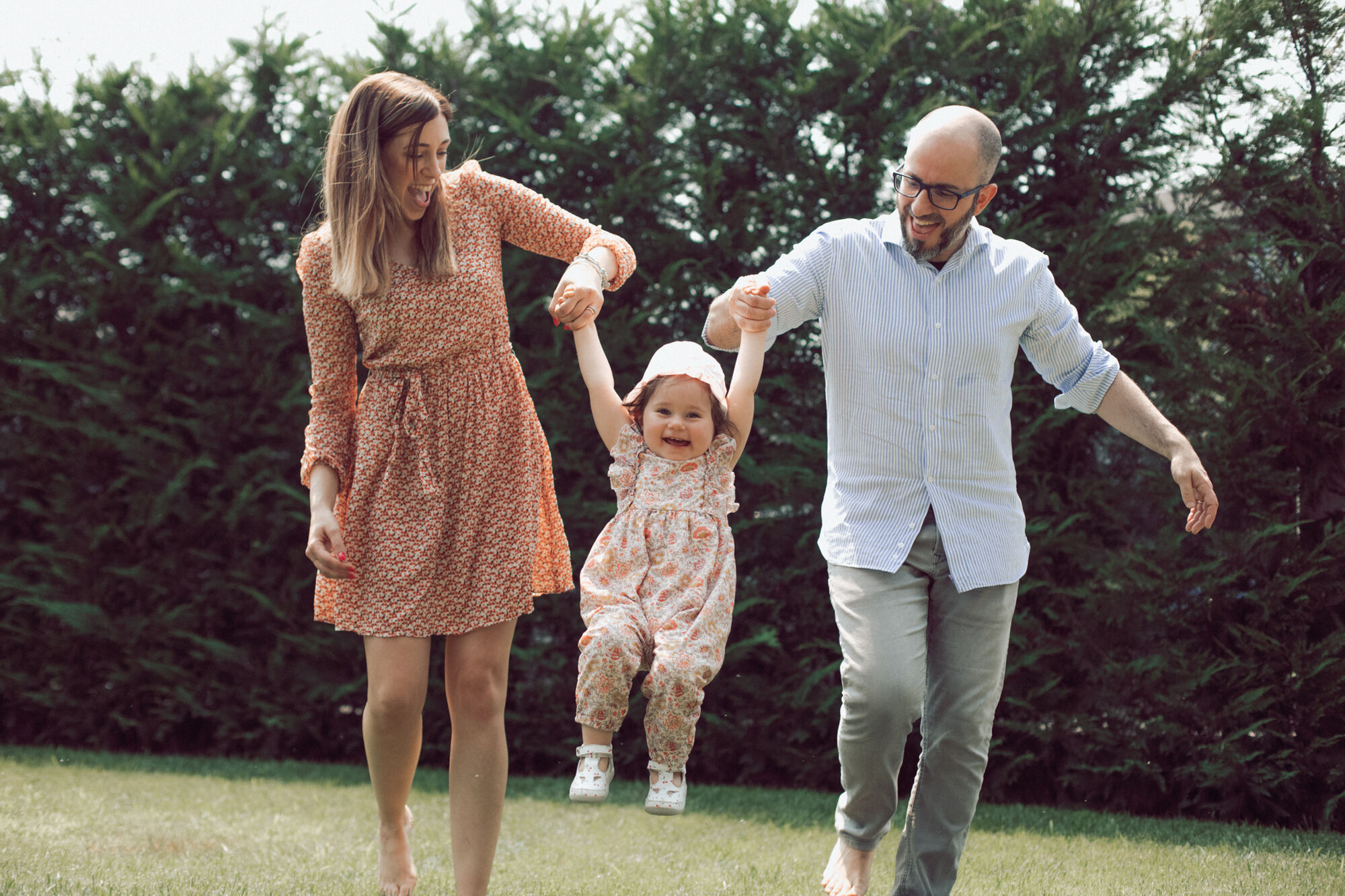 Mamma e papà tengono per mano la bimba che salta in giardino