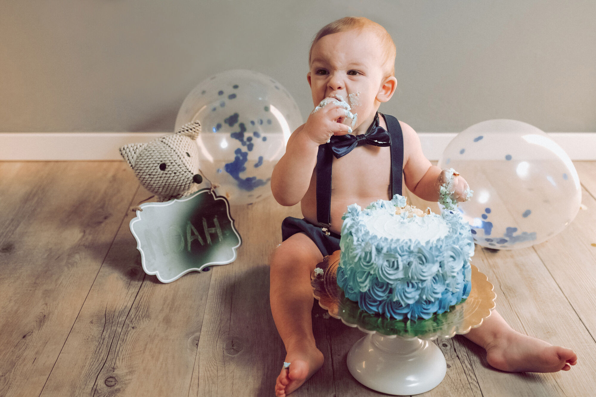 Bimbo con papillon e bretelle assaggia una torta azzurra tra palloncini, smash cake per il primo compleanno
