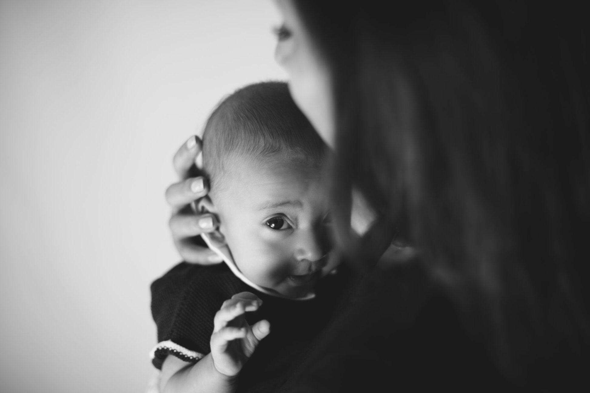 Neonato in braccio alla mamma guarda in camera, ritratto intimo in bianco e nero, foto neonato a casa