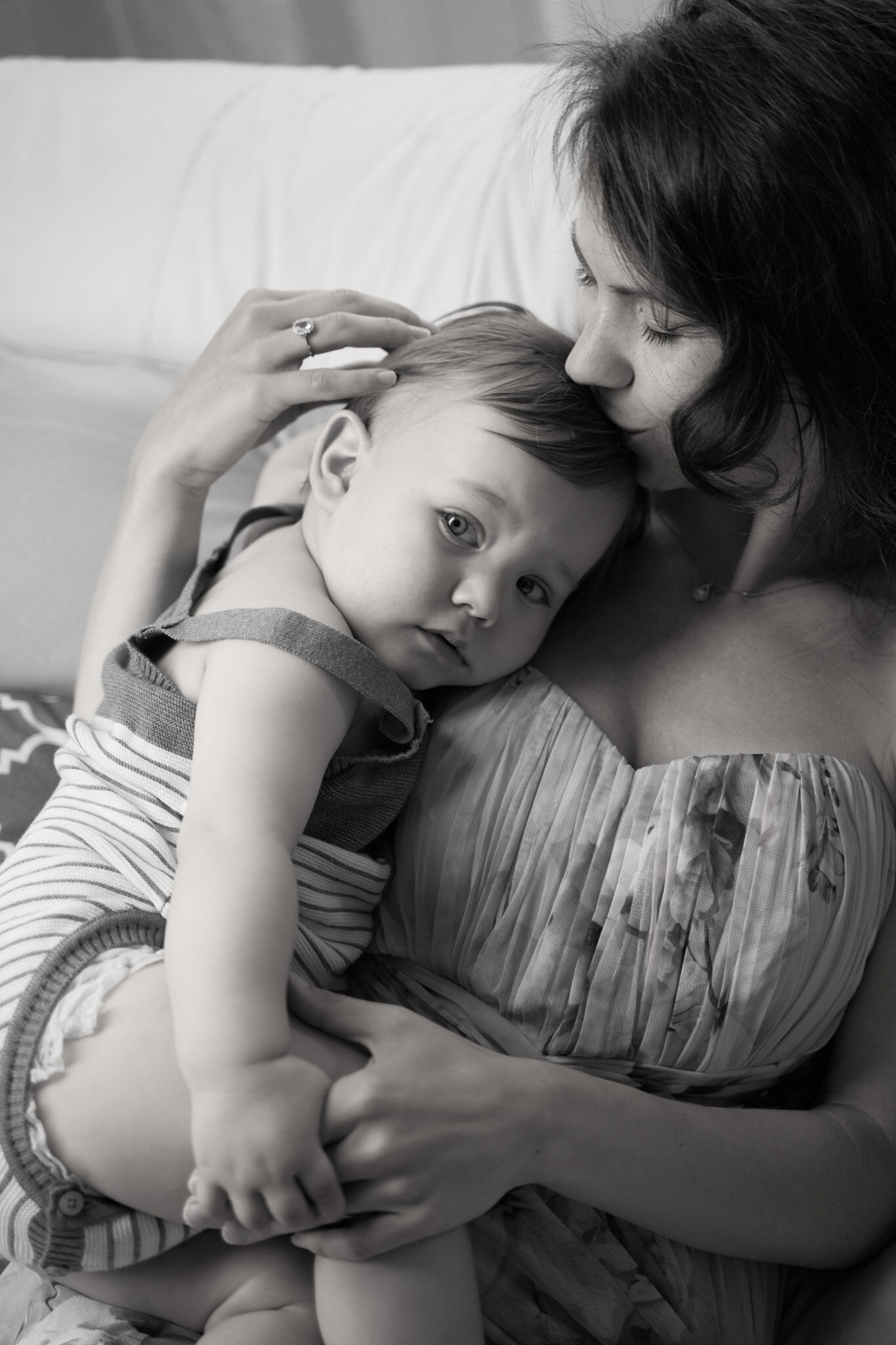 Mamma bacia sulla testa il suo bimbo appoggiato al petto sul divano, foto di famiglia in bianco e nero