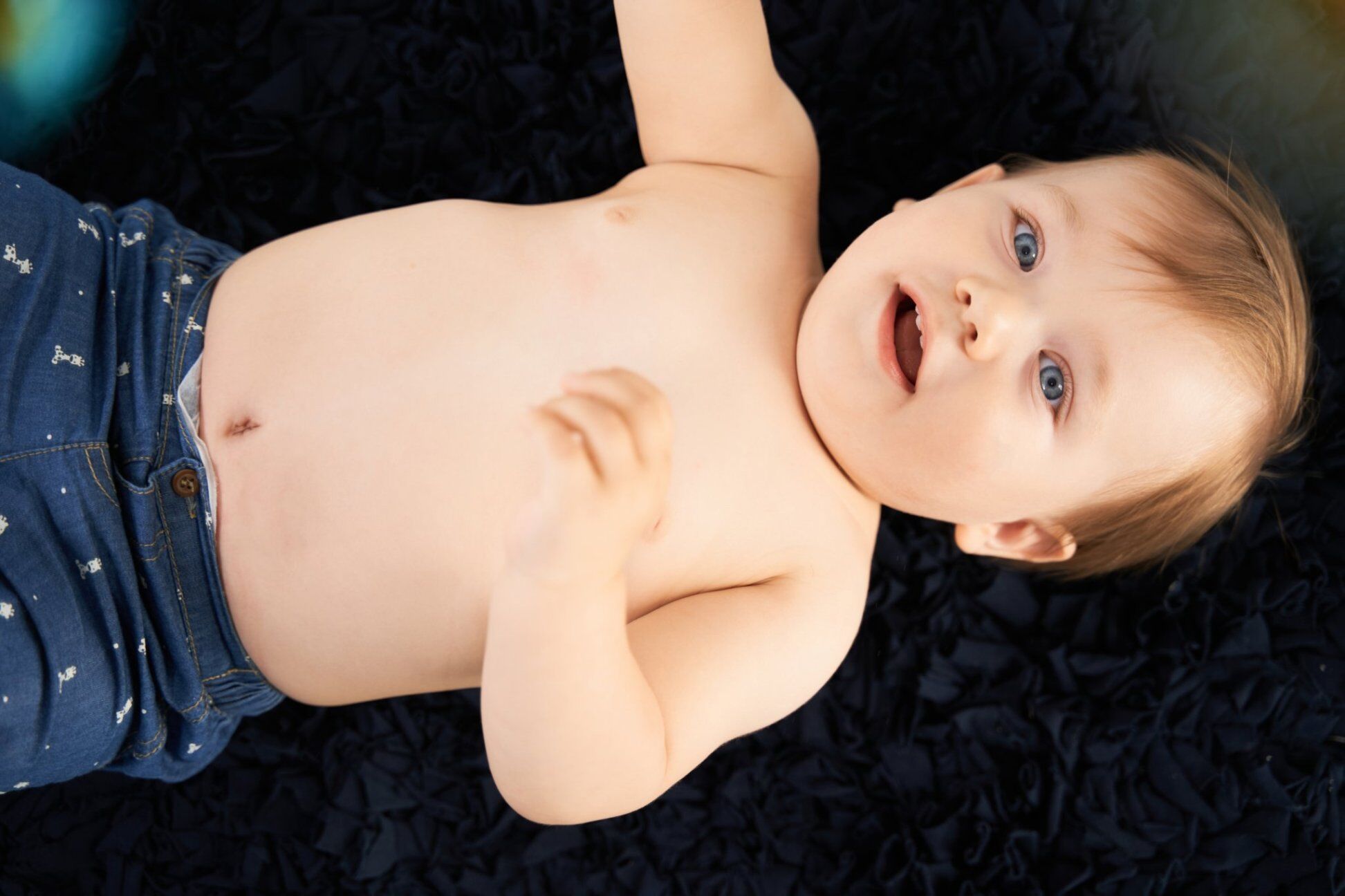 Bimbo sdraiato su tappeto scuro guarda in alto a bocca aperta, ritratto a colori del servizio fotografico bambini