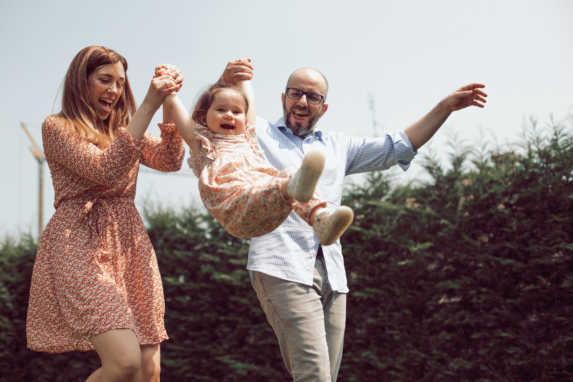 Mamma e papà sollevano in aria la figlia ridente tenendola per le mani all'aperto, foto di famiglia spontanea