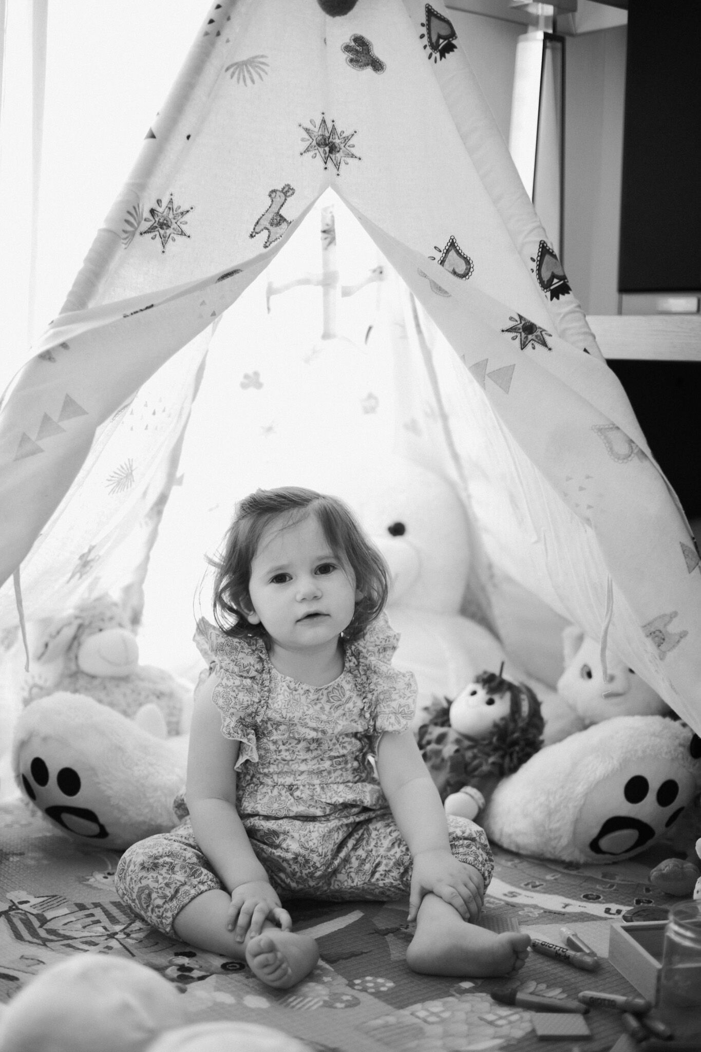 Bimba seduta davanti a una tenda tipi con i peluche, in bianco e nero