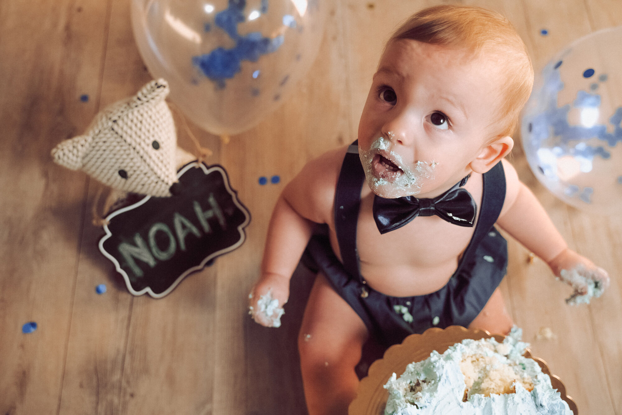 Bimbo con la bocca sporca di panna guarda in alto stupito, servizio fotografico bambini con torta e coriandoli blu