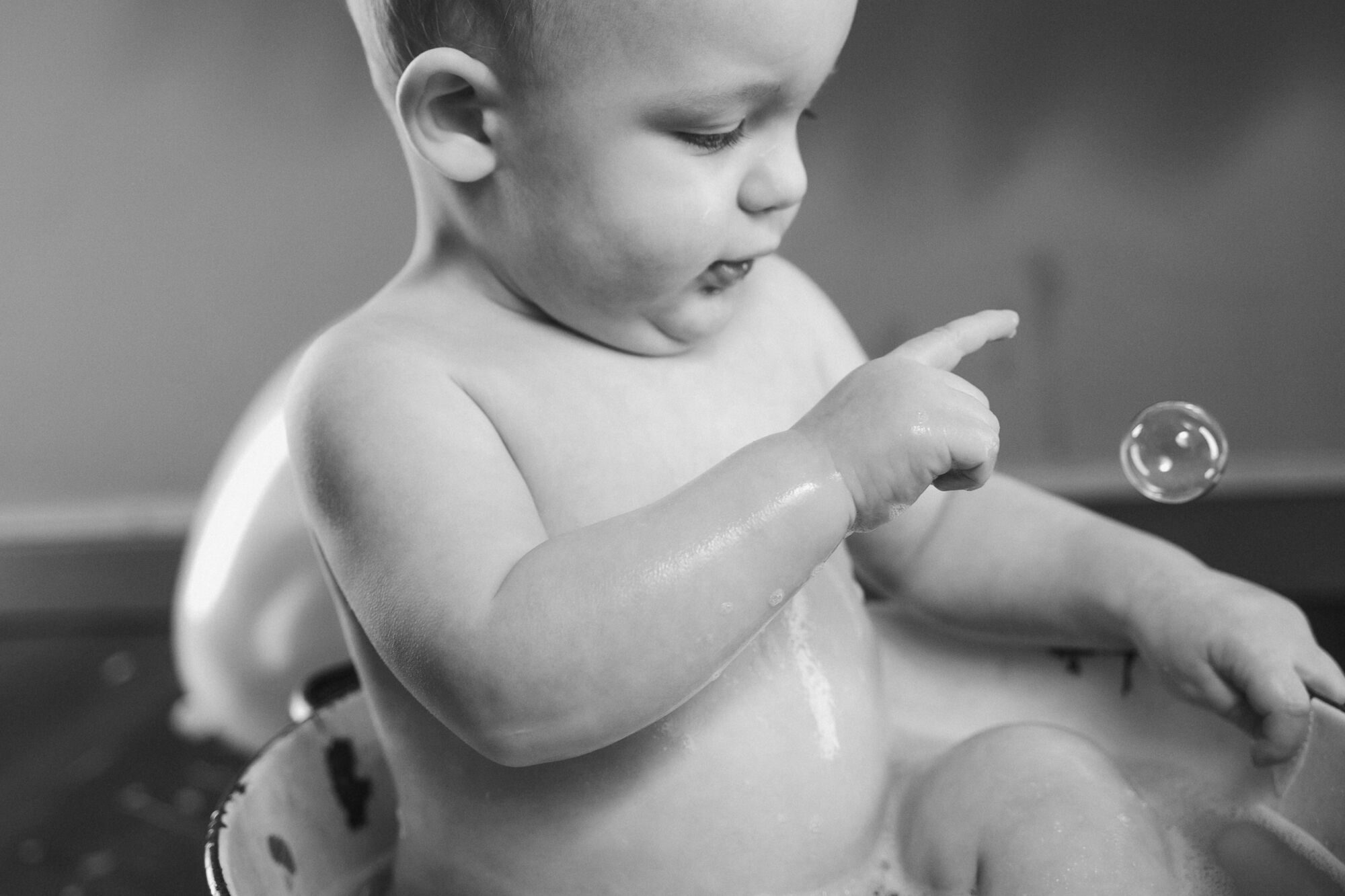 Bianco e nero di un bimbo nel bagnetto che indica una bolla di sapone, servizio fotografico bambini