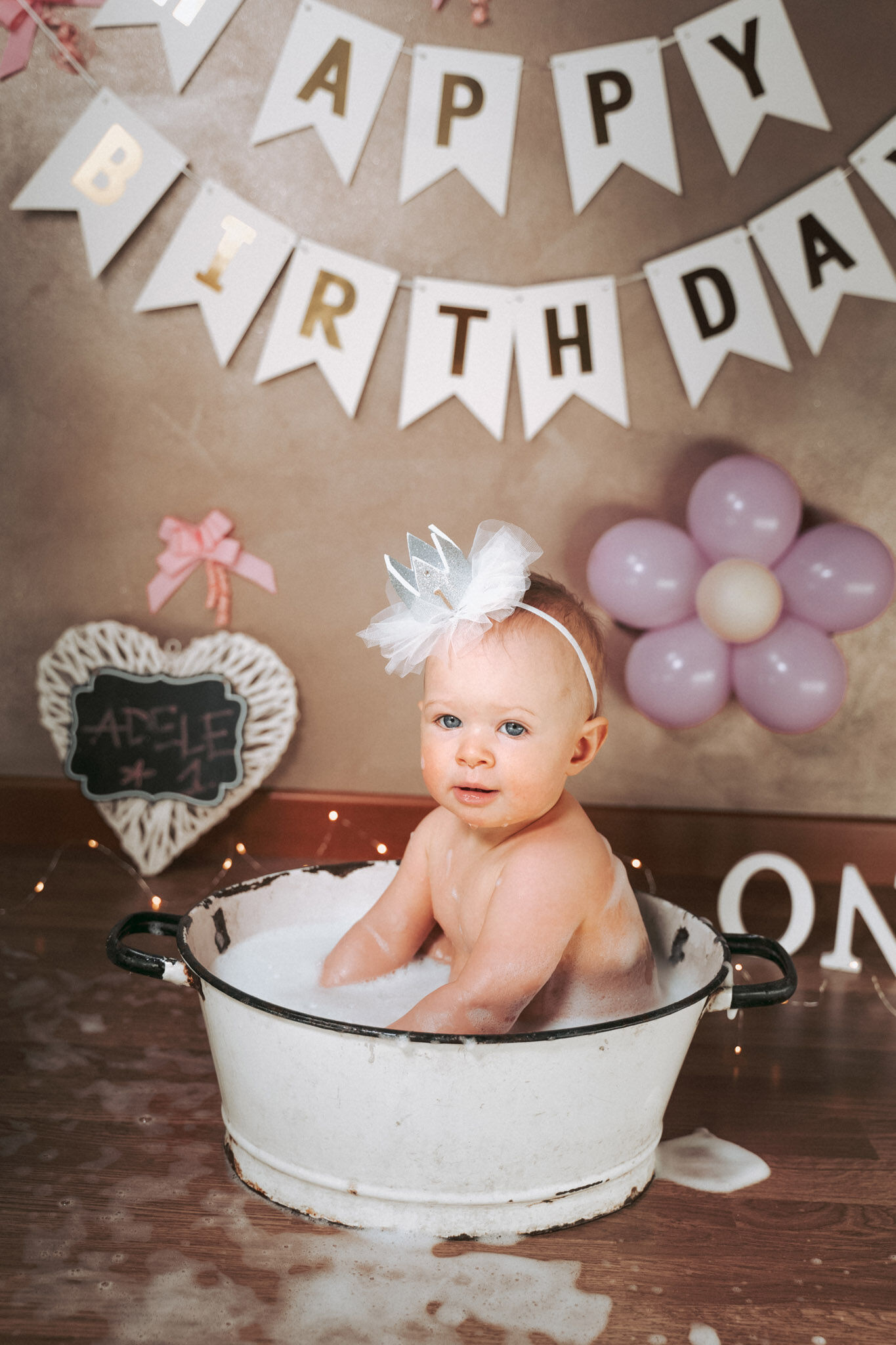 Bimba con fiocco di tulle nella tinozza bianca, palloncini rosa a fiore e festone di compleanno, smash cake