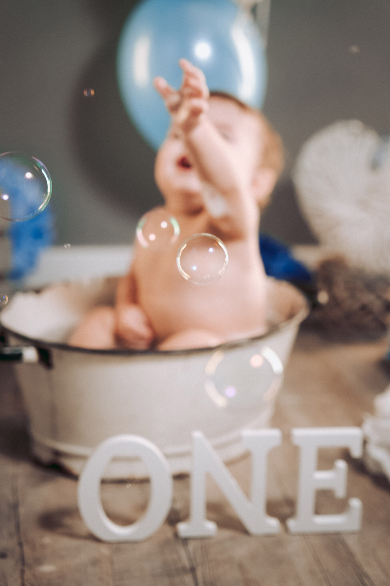 Bolle di sapone a fuoco davanti a un bimbo sfocato nella tinozza, scritta ONE in primo piano, primo compleanno