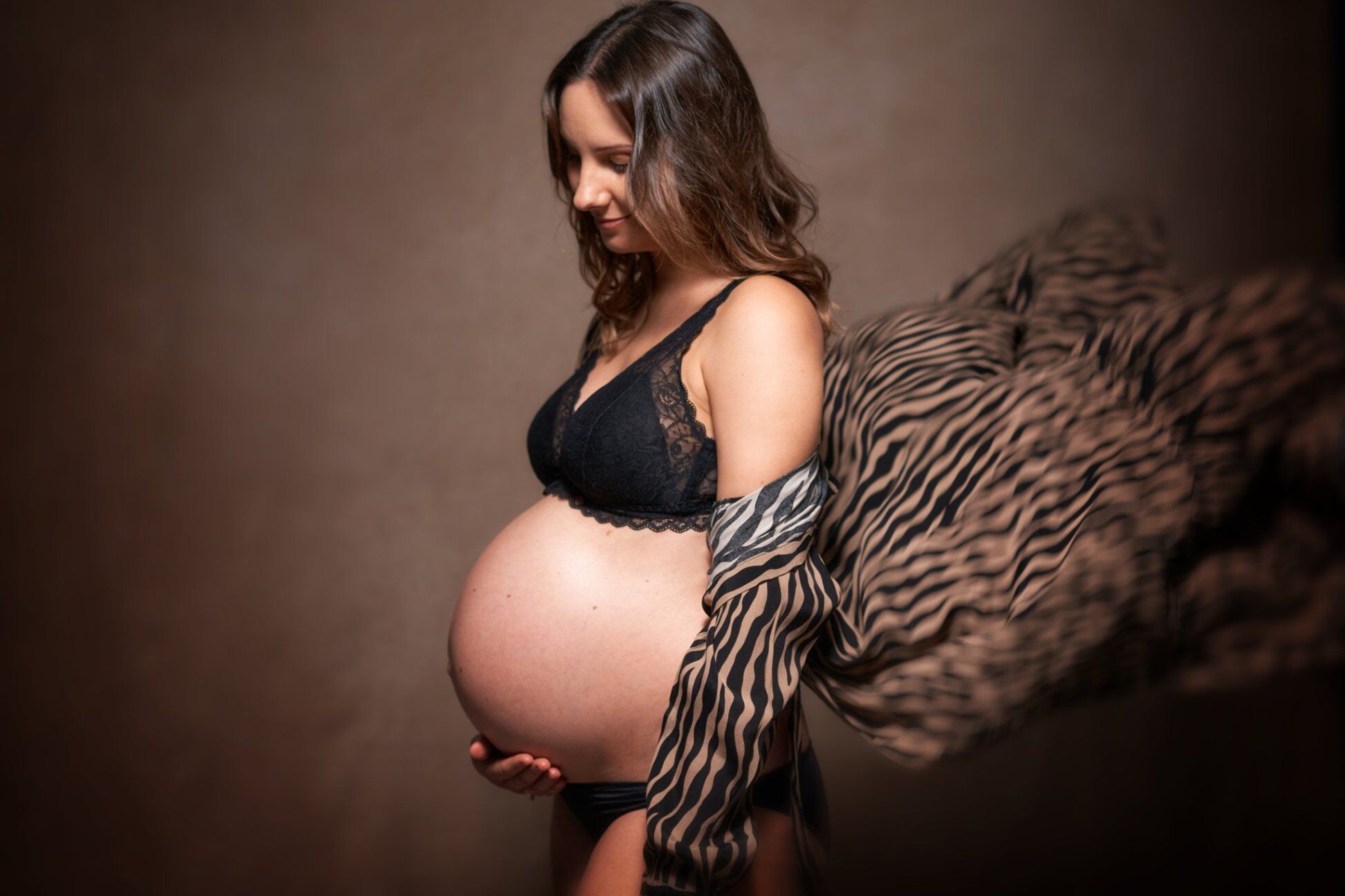 Futura mamma in reggiseno nero con telo zebrato al vento, servizio fotografico gravidanza su fondo marrone