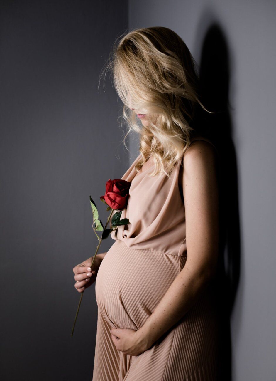 Mamma in abito rosa con una rosa in mano, fondale grigio in studio