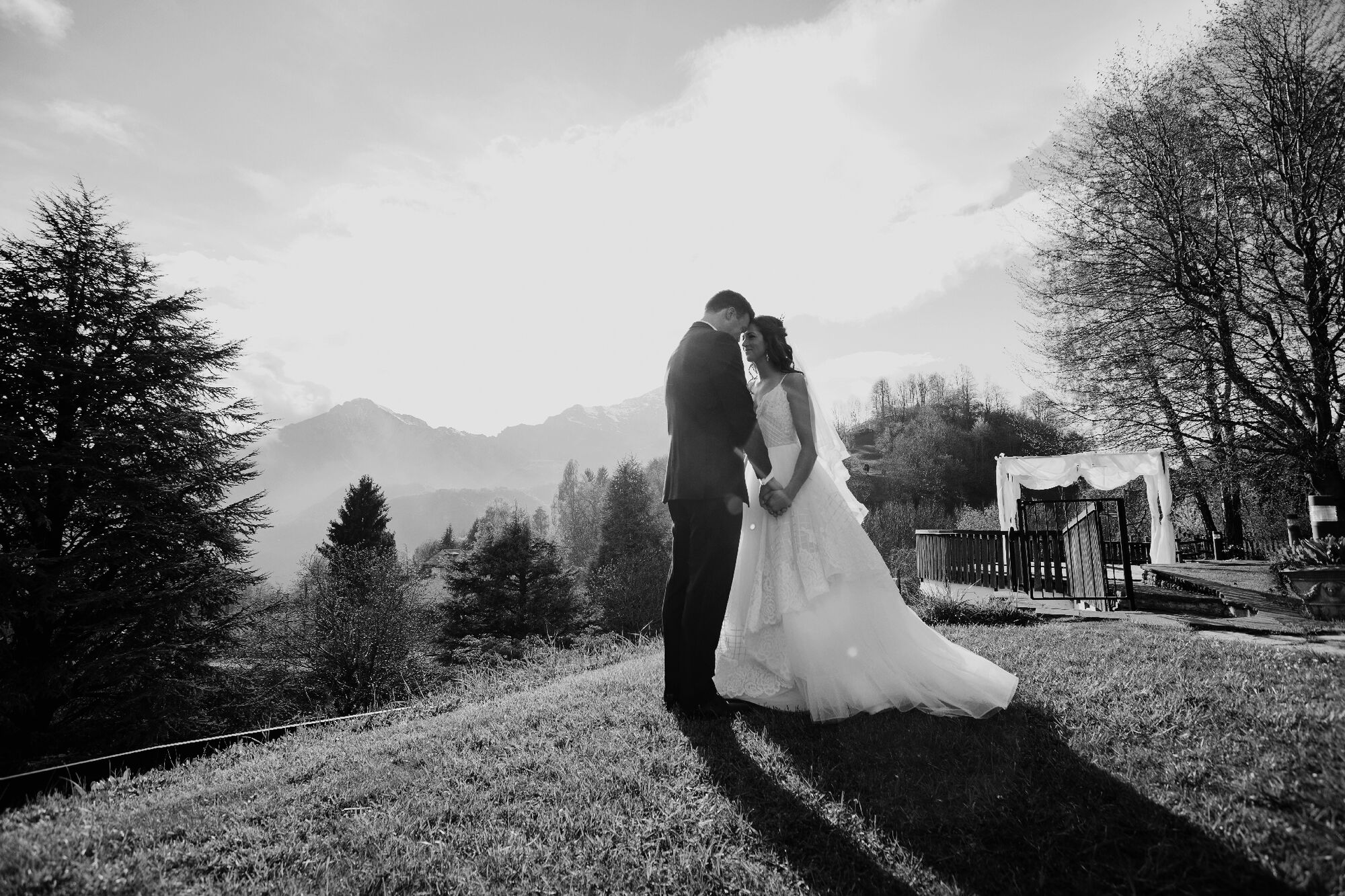 Sposi fronte a fronte su un prato collinare con montagne sullo sfondo, foto di matrimonio in bianco e nero