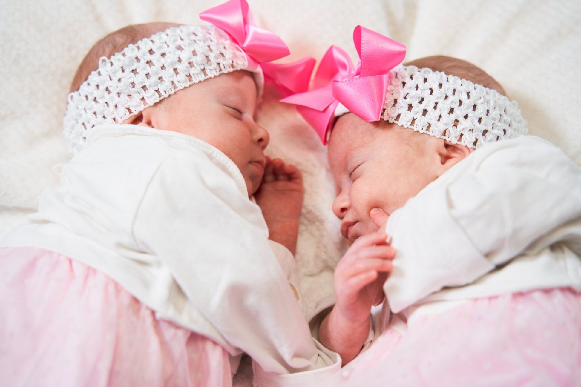 Due gemelline addormentate viso a viso con fasce e fiocchi rosa, servizio fotografico newborn